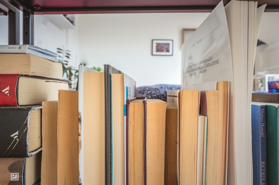 Stack of books on a shelf with a laptop nearby